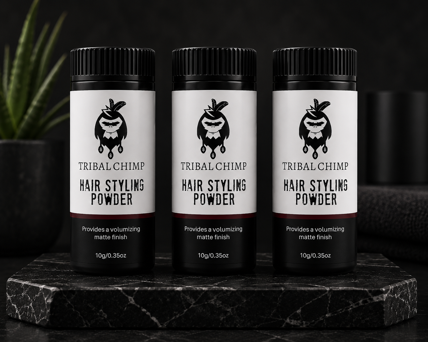 Three bottles of Tribal Chimp Hair Styling Powder on a dark surface with a plant in the background. Buy 2  Receive 1 Complimentary.
